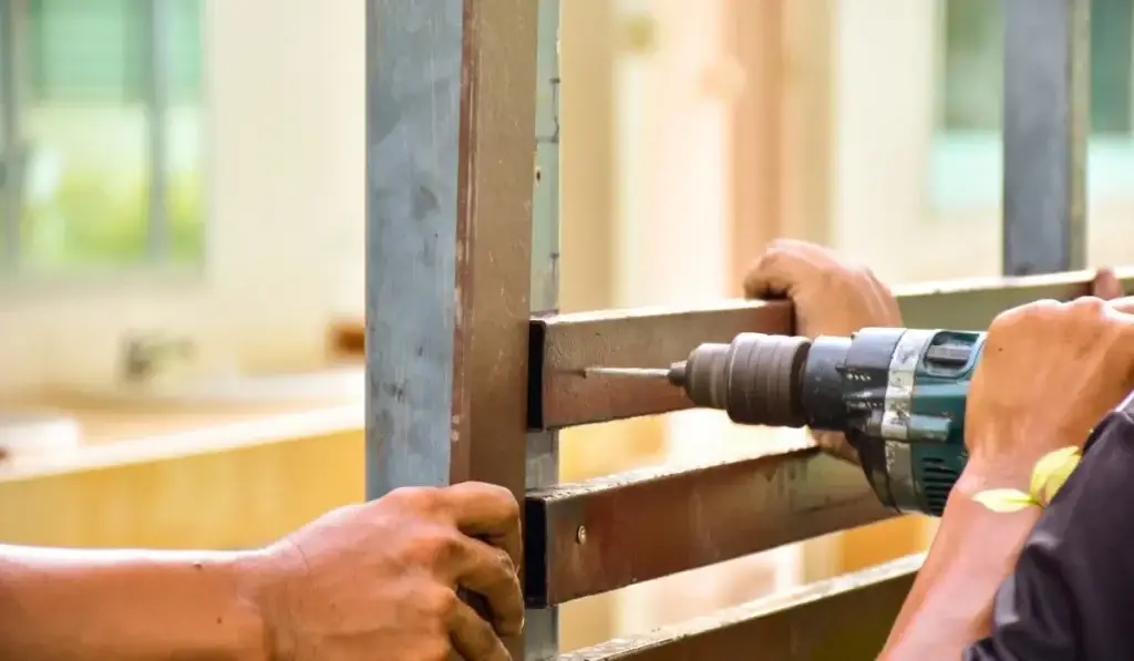 Hands using a power drill for DIY fence installation, securing metal frame for home improvement project.