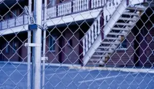 Close-up of locked chain-link fence gate in front of brick apartment, showing chain-link vs. steel fencing.