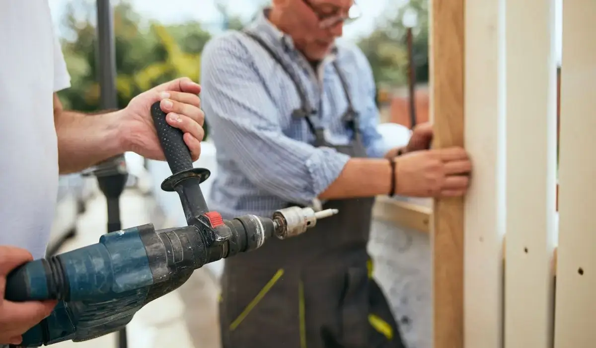 Two contractors preparing wood fence posts with a power drill during a new fence installation in a residential Chicago neighborhood.