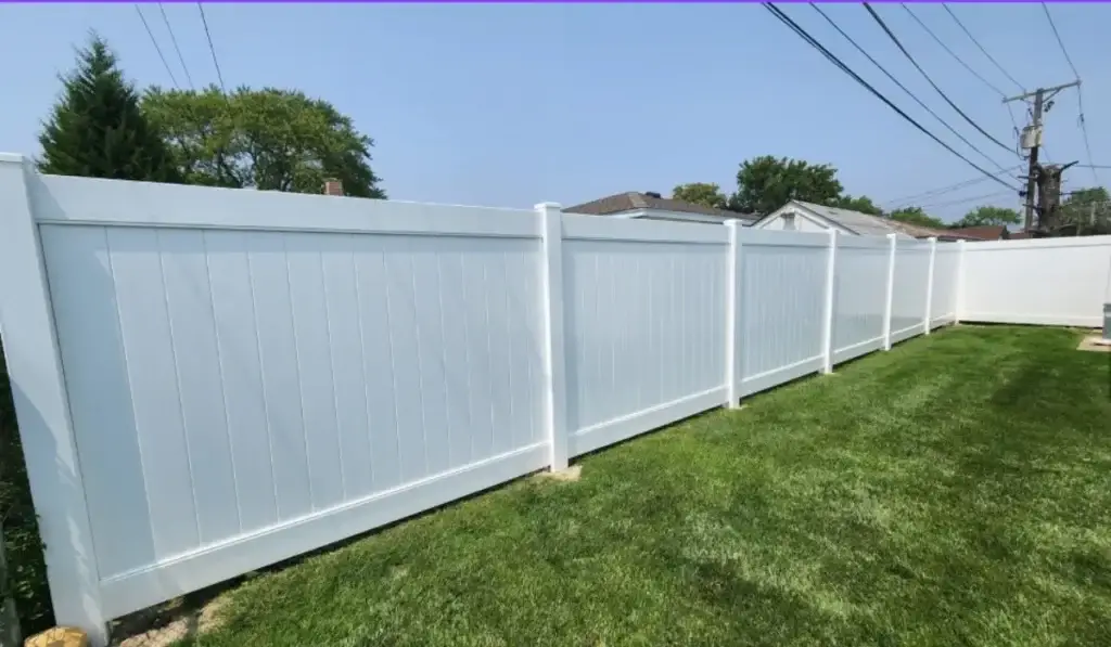 Newly installed white vinyl privacy fence on green lawn under clear sky in a Chicago residential yard.