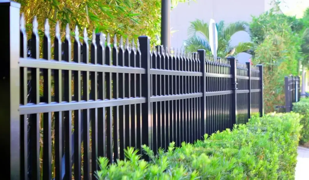 Black metal security fencing with anti-climb spikes in landscaped area.