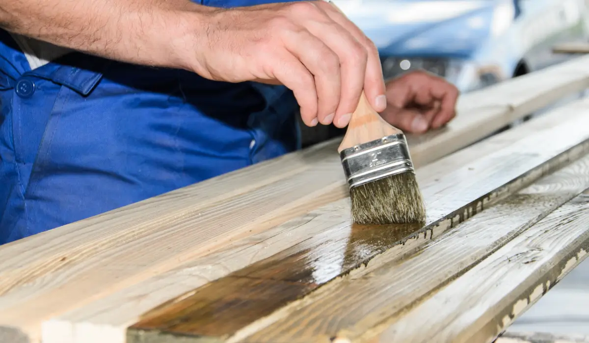 Close-up of a worker applying protective sealant with a brush on wooden fence boards to prepare for a harsh winter.